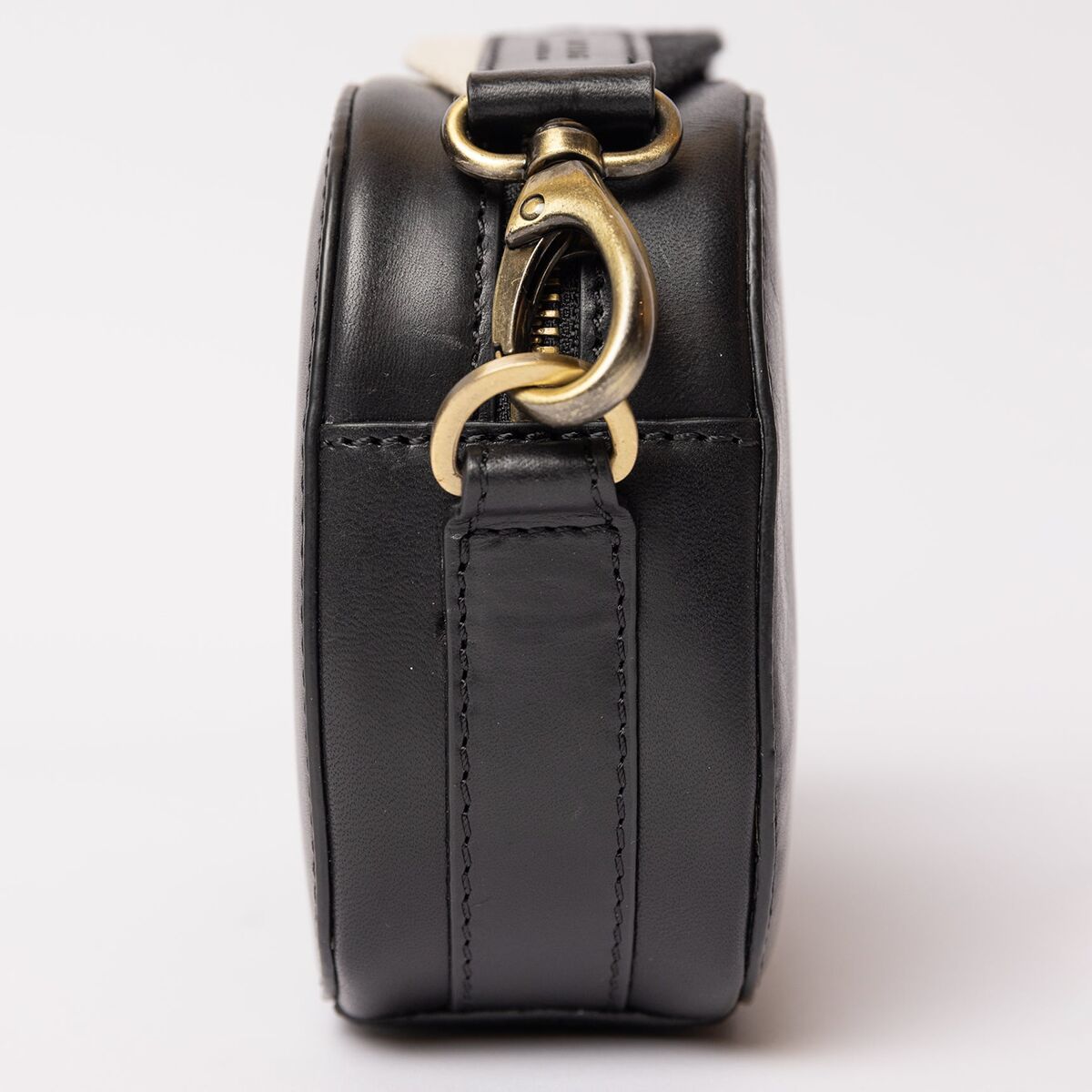 Seitliche Nahaufnahme einer eleganten Umhängetasche »Maya« aus schwarzem Material mit goldfarbenem Metallverschluss, neutraler Hintergrund.