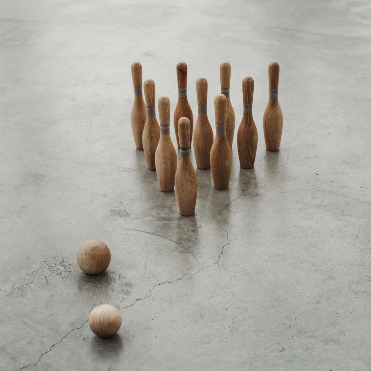 Ein Holzkegel-Set auf einem grauen Boden. Es gibt zwei Holzkugeln und eine Gruppe von neun Holzkegeln, die in einem Dreieck aufgestellt sind.