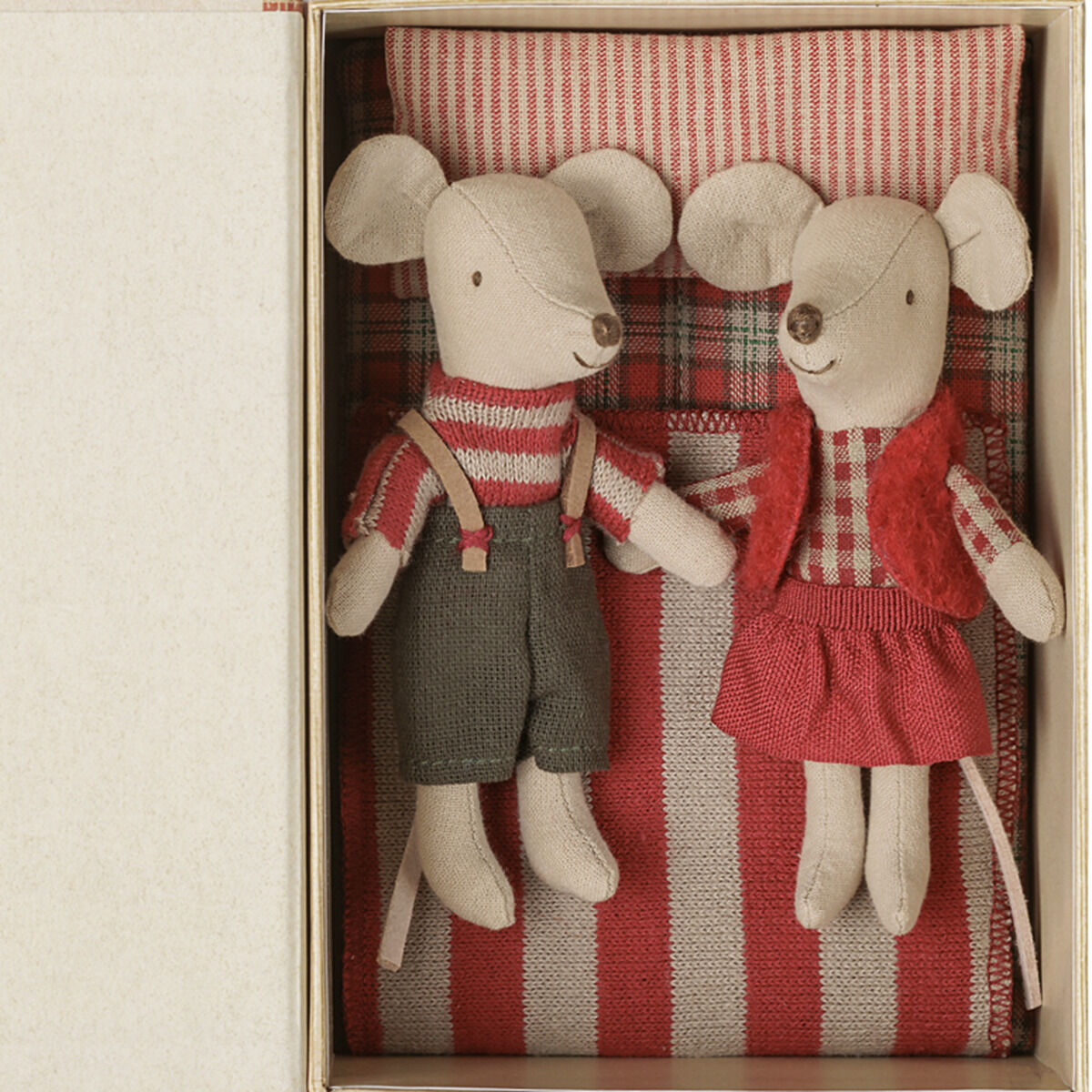 Zwei Kuschelmäuse mit gestreifter Kleidung und roten Akzenten liegen nebeneinander in einem Bett mit gestreifter Bettwäsche und Kissen, alles arrangiert in einer beigefarbenen Box im Buchformat. Die Szenenfarben wirken harmonisch und festlich.