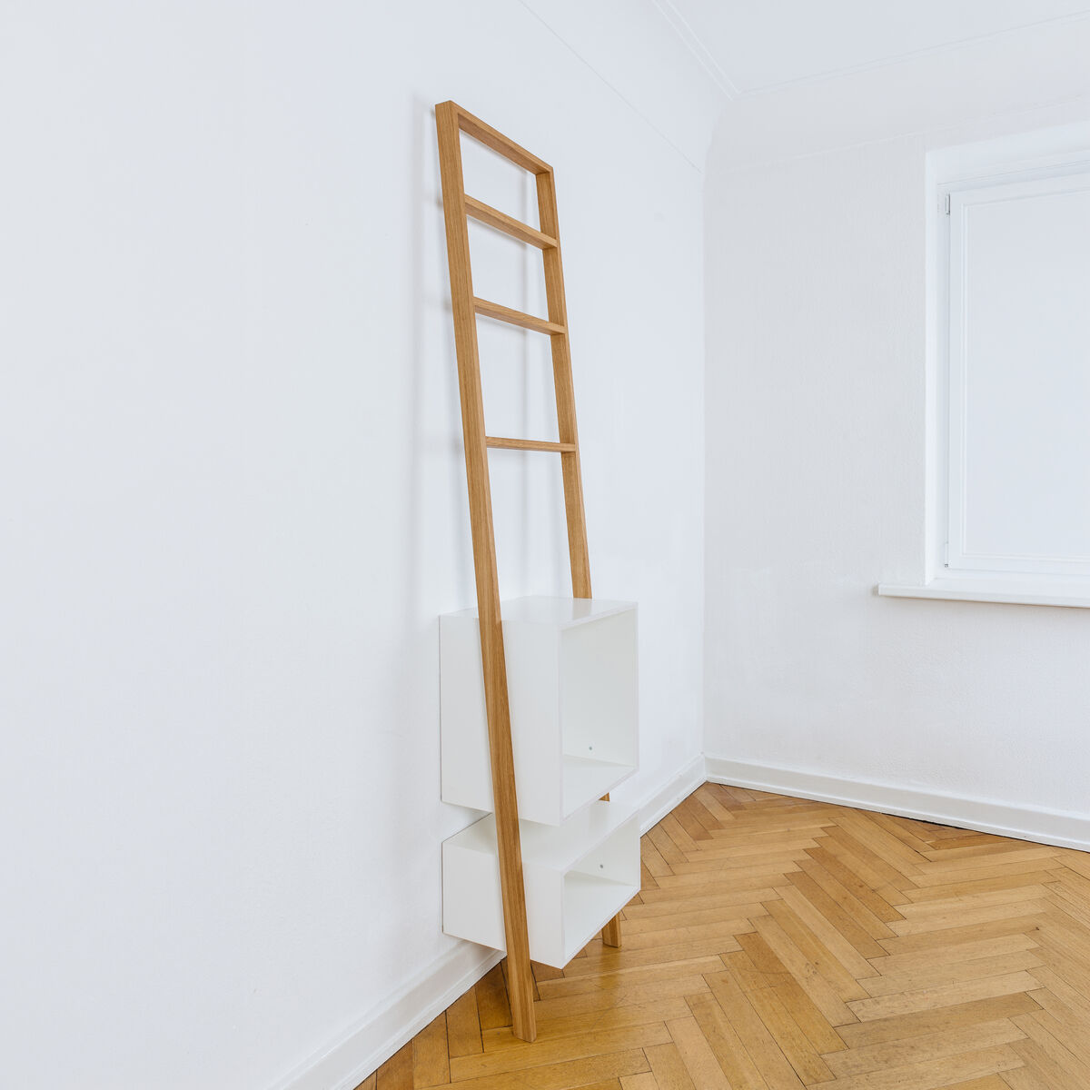 Das Leiterregal »brecht« von das kleine b lehnt an einer weißen Wand auf Parkettboden. Es besteht aus geölter Eiche mit drei weißen, matten Regalkästen und minimalistischer, filigraner Gestaltung. Ideal für Bücher, Deko oder Schallplatten in modernen, kleinen Räumen.