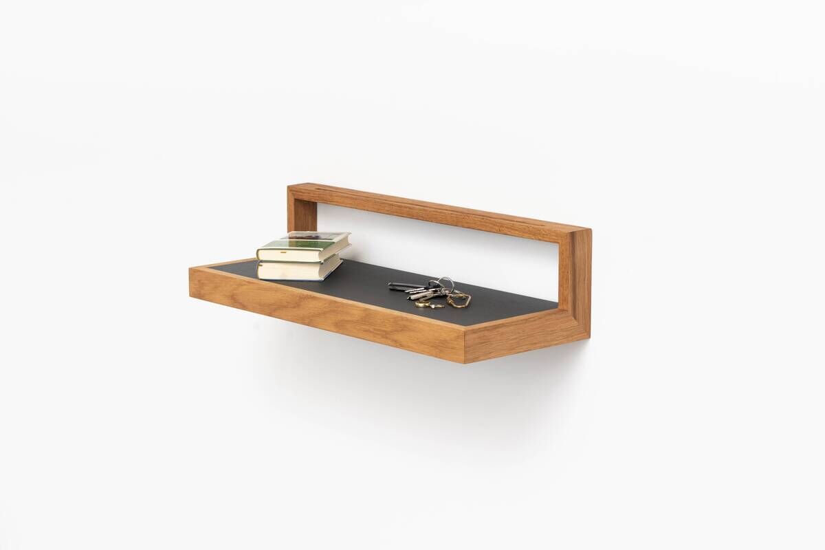 Ablagebord 'buck' in Anthrazit, montiert an einer weißen Wand und aus Holz, mit Büchern und Schlüsseln darauf.