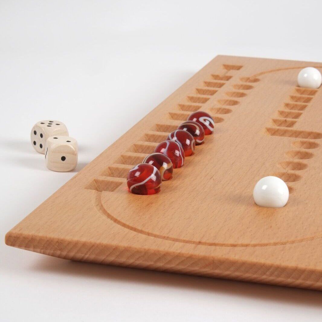 Das Bild zeigt ein Holzbrettspiel namens Spiel Samsara. Das Spielbrett besteht aus hellem Holz mit eingravierten Spielpfaden, auf denen mehrere rote und weiße Murmeln platziert sind. Zwei weiße Würfel sind ebenfalls sichtbar.