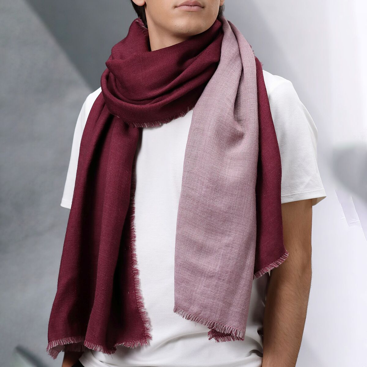 Ein zweifarbiger Wollschal Modell »Carla« in Doubleface-Optik mit den Farbtönen Weinrot und Rosé, locker um den Hals einer Person gelegt, vor neutralem Hintergrund. Das Design vereint klassische Eleganz und Wärme für kühle Tage.