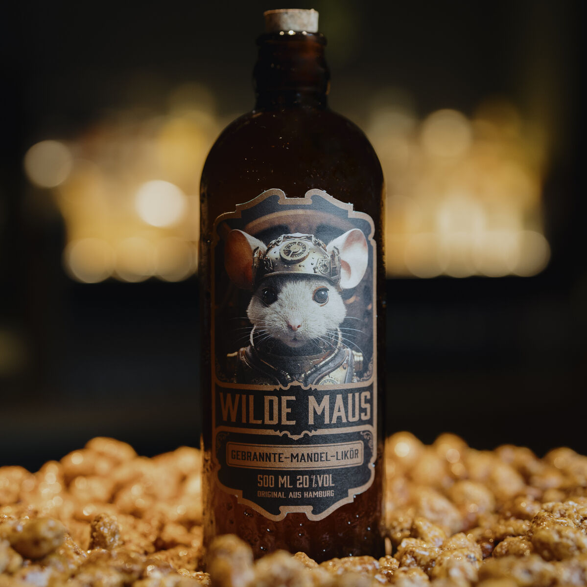 Eine braune Flasche des Mandel-Likörs »Die wilde Maus«, umgeben von gebrannten Mandeln. Das Etikett zeigt eine Maus in traditioneller bayerischer Kleidung.