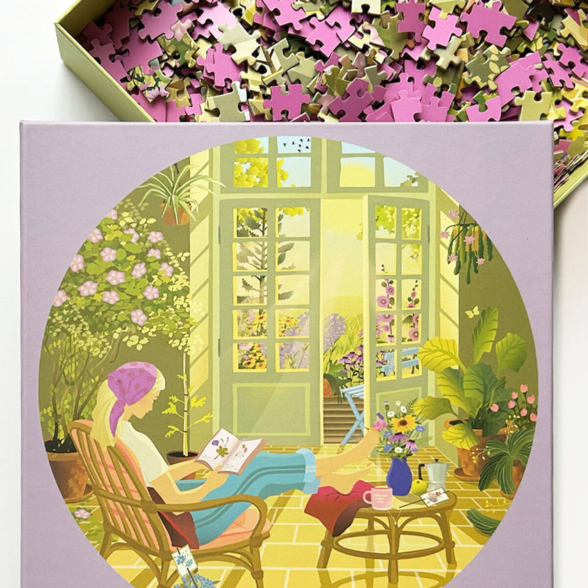 Das 1000-Teile Puzzle »Morning Glow« der Marke VISSEVASSE zeigt eine stilisierte Szene: Eine Person liest in einem sonnendurchfluteten Raum voller Pflanzen. Der Karton ist geöffnet, Puzzleteile in Rosa und Gelb sichtbar. Stimmungsvolles, gemütliches Motiv.