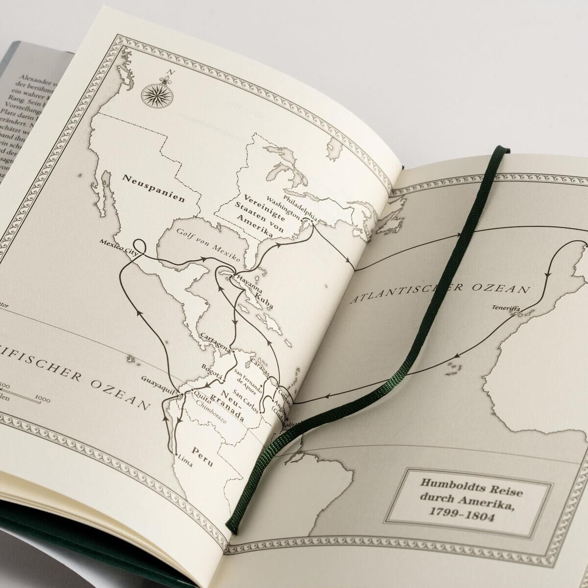 Ein aufgeschlagenes Buch mit dem Titel 'Wulf, A: Alexander von Humboldt und die Erfindung der Natur'. Es zeigt eine historische Karte von Südamerika und dem Atlantischen Ozean. Ein grünes Lesezeichen ist zwischen den Seiten platziert.