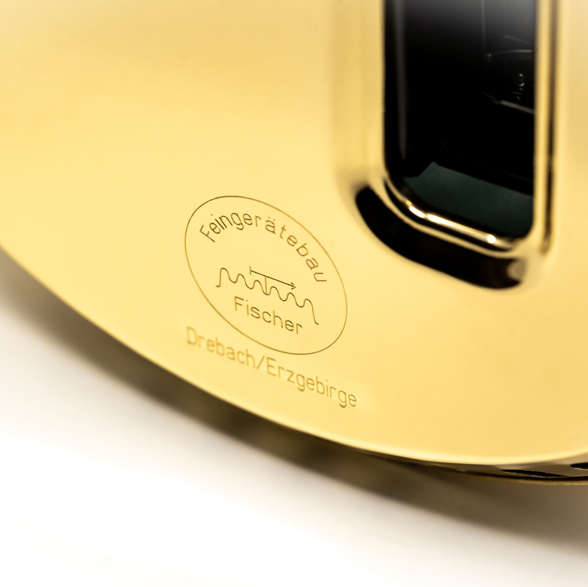 Nahaufnahme einer Weltzeituhr aus der ZEIT-Sonderedition »POLAR Weltzeituhr« von Fischer Manufaktur. Das Bild zeigt die Prägung des Herstellers mit Fokus auf dem goldfarbenen Metall und einigen schwarzen Details.