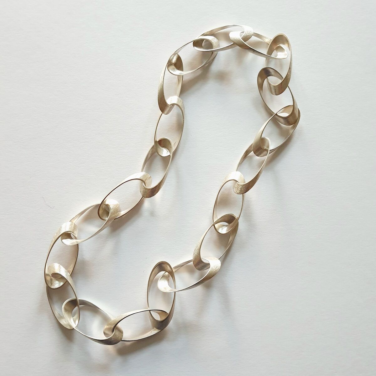Eine elegante Halskette mit großen, ovalen Gliedern in Gold, die auf einem weißen Hintergrund liegt. Das Design wirkt modern und minimalistisch.