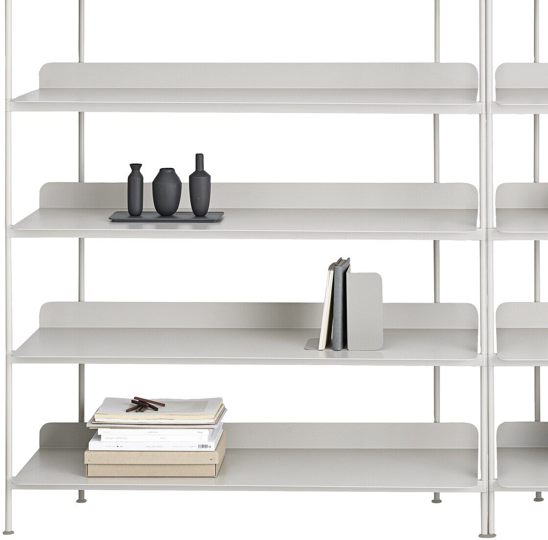 Das Bild zeigt ein modernes Bücherregal mit mehreren weißen Regalböden, auf denen Bücher, Vasen, ein Krug und weitere Dekorationsgegenstände ordentlich aufgestellt sind. Die Regalböden und Gegenstände sind in neutralen Farben wie Weiß, Beige, Grau und Schwarz gehalten.