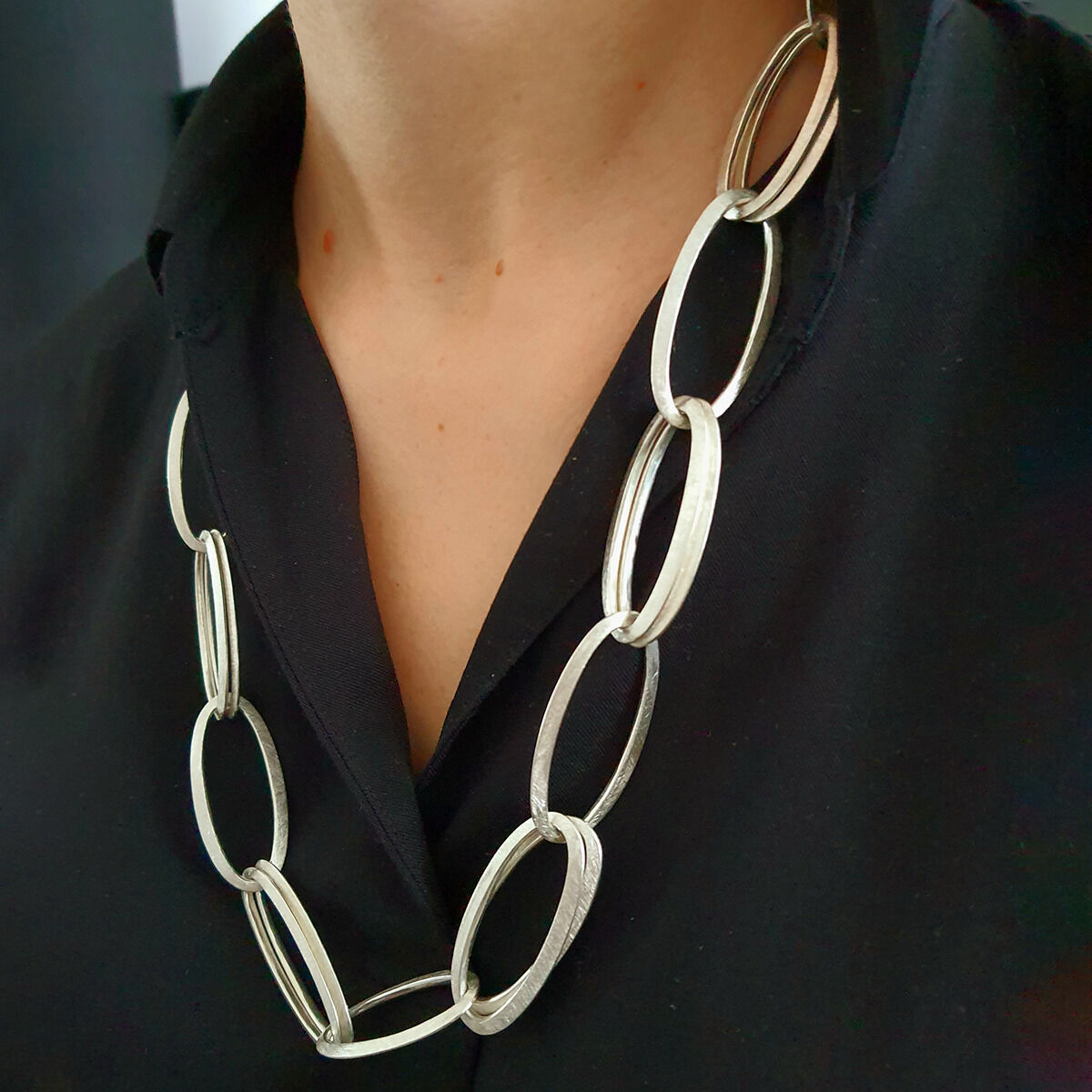 Großgliederiges, handgefertigtes Collier »GRACE« aus 925er Silber der Marke HML Berlin an einem Hals, getragen zu schwarzer Kleidung. Die Kette besteht aus großen, ovalen, mattierten Gliedern und erzeugt einen eleganten, zeitlos-modernen Look.