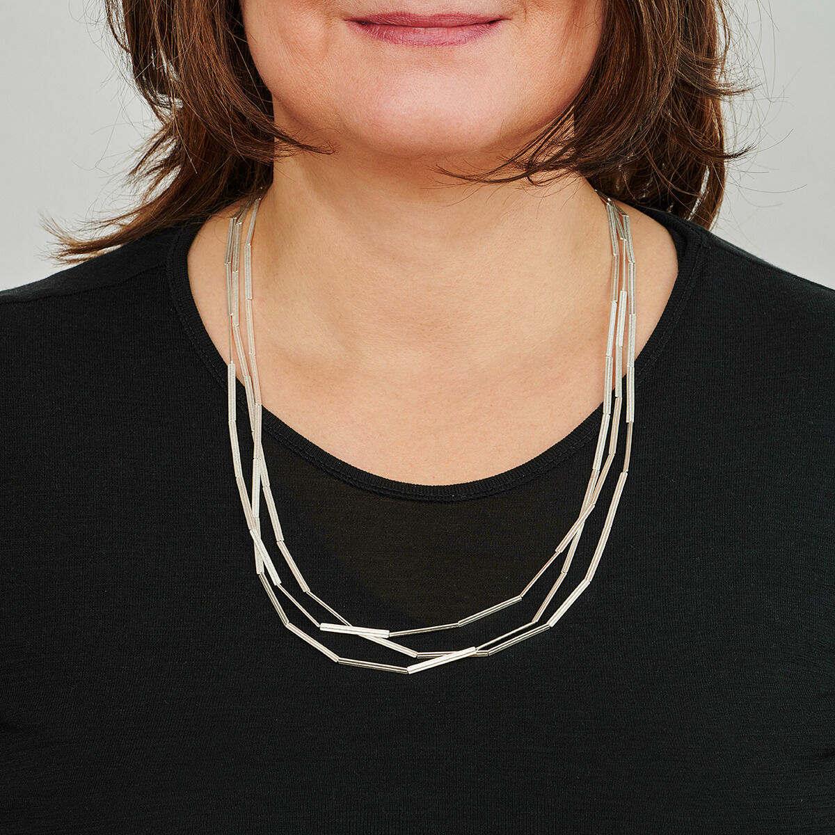 Eine Frau trägt eine silberne Kette mit Streifenmuster auf einem schwarzen Oberteil.