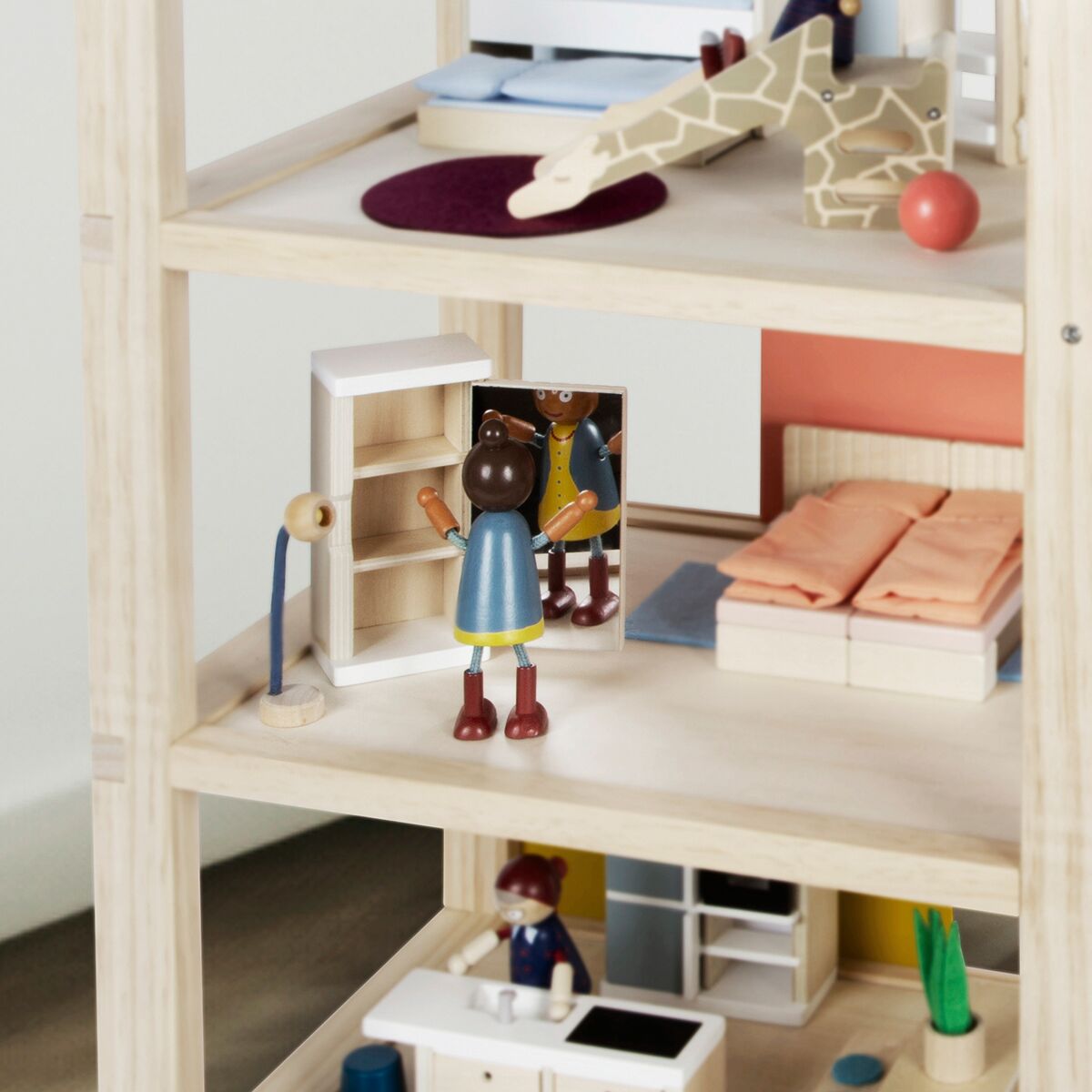 Modernes Puppenhaus aus Holz mit mehreren Etagen, vollständig eingerichtet mit Miniaturmöbeln. Kinderfiguren stehen im Wohnzimmer neben einem offenen Regal. Im Hintergrund sind Möbel wie ein Bett, eine Rutsche und weitere Dekoelemente sichtbar. Das Puppenhaus eignet sich perfekt zum kreativen Spielen und als schönes Geschenk für Kinder.