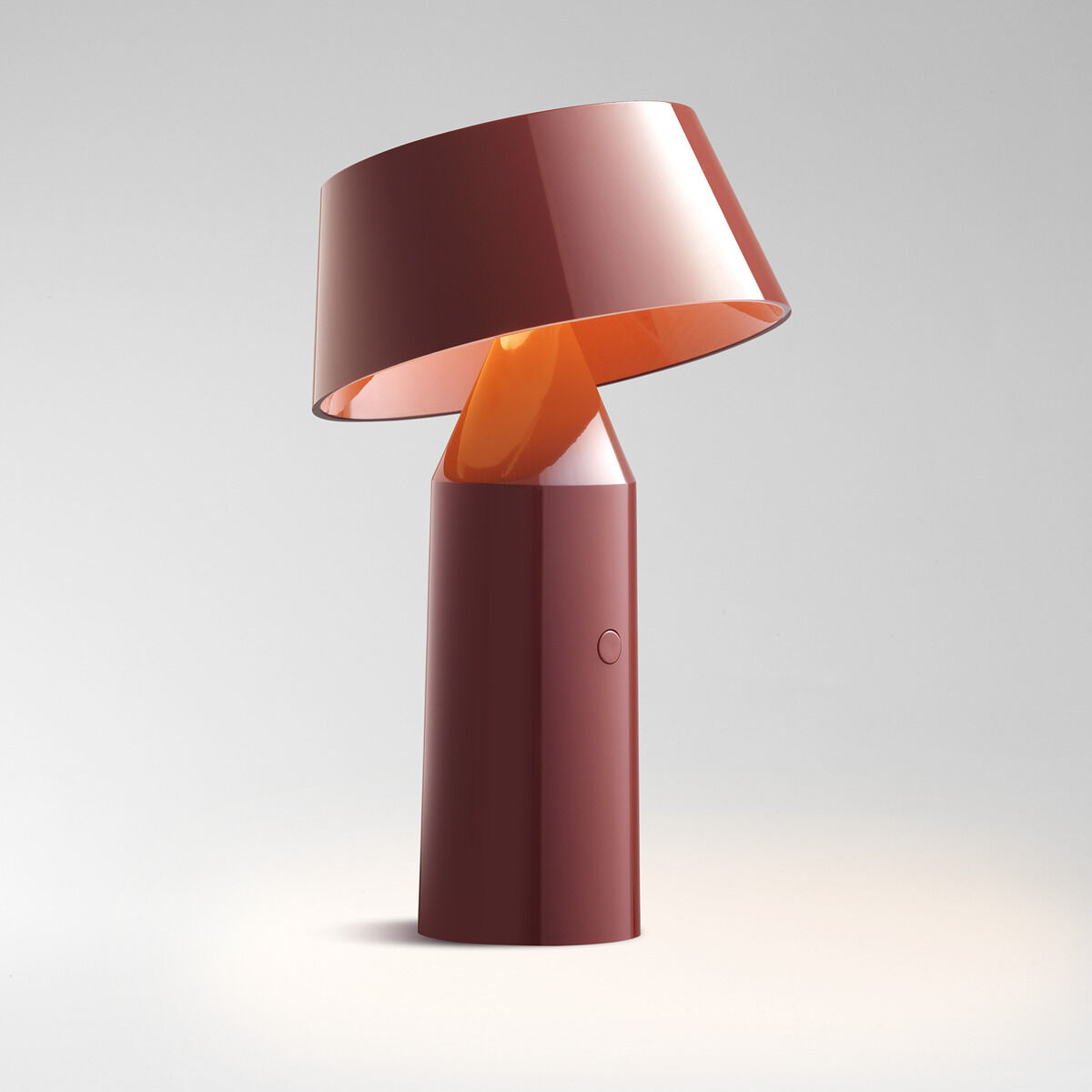 Eine moderne Tischleuchte in Bordeaux und Orange mit minimalistischer Ästhetik. Die Lampe hat einen geneigten Schirm, der auf einem zylinderförmigen Sockel sitzt. Sie strahlt ein warmes Licht aus.