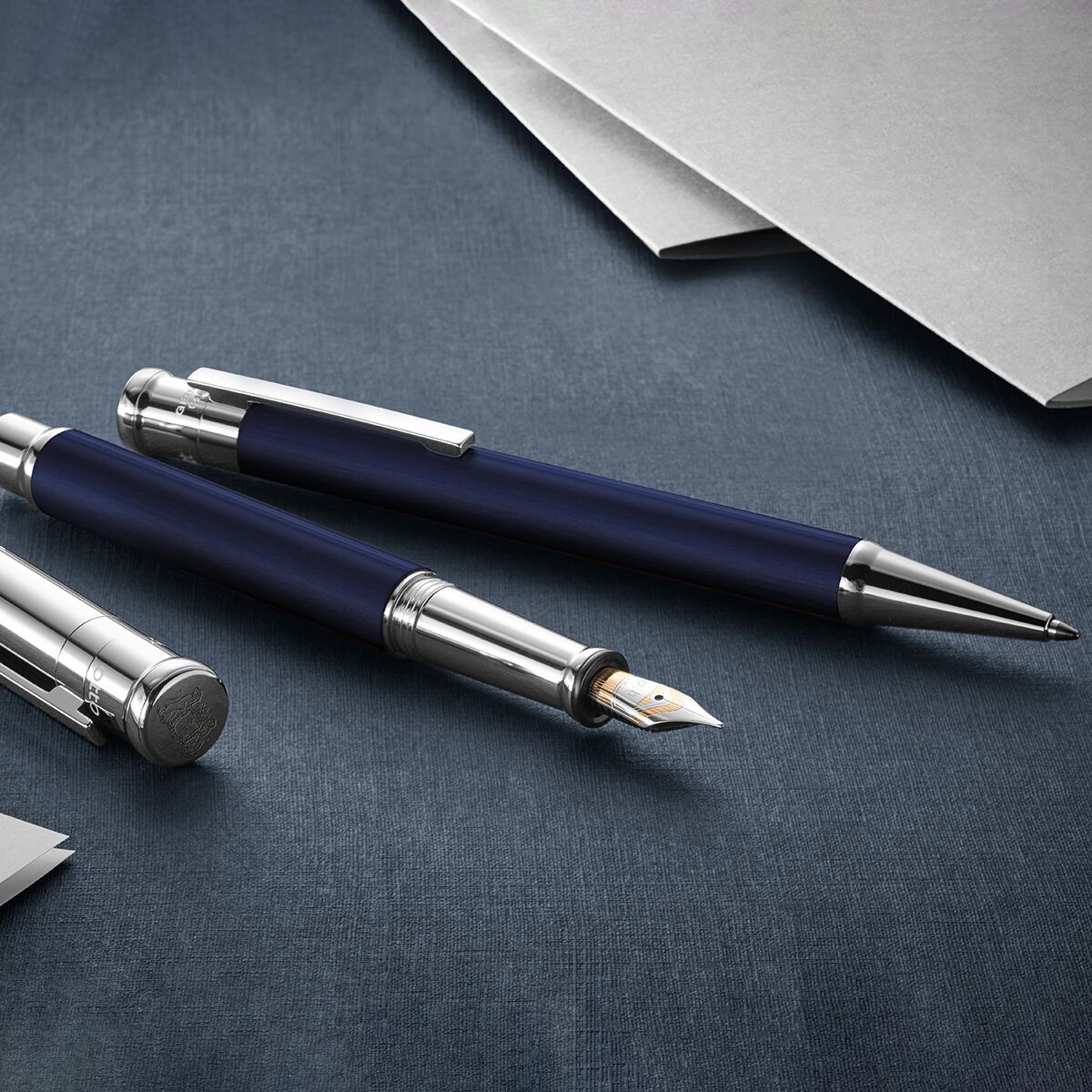 Ein hochwertiger Kugelschreiber der ZEIT Sonderedition Design 04 liegt auf einem dunkelblauen Stoff, umgeben von silbernen und weißen Papierbögen. Der Stift zeichnet sich durch ein elegantes, modernes Design mit Metallakzenten aus.