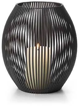 Ein Windlicht aus schwarzem Metall mit eleganten, vertikalen Streben. Im Inneren befindet sich eine brennende, weiße Kerze, die warmes, cremefarbenes Licht ausstrahlt.