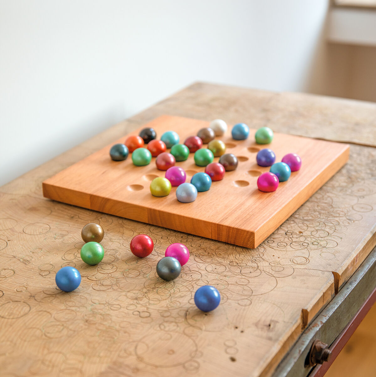 Holzbrettspiel Solitär auf einem rustikalen Tisch mit bunten Kugeln.