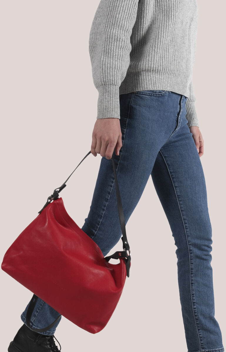 Eine Person in blauer Jeans und grauem Pullover trägt eine rote Lederschultertasche 'Nabuko'.