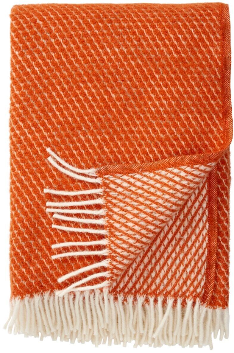 Das Bild zeigt die Decke »Velvet«, eine kuschelige und weiche Decke mit orange-weißem Muster und weißen Fransen, ideal für gemütliche Abende auf dem Sofa.