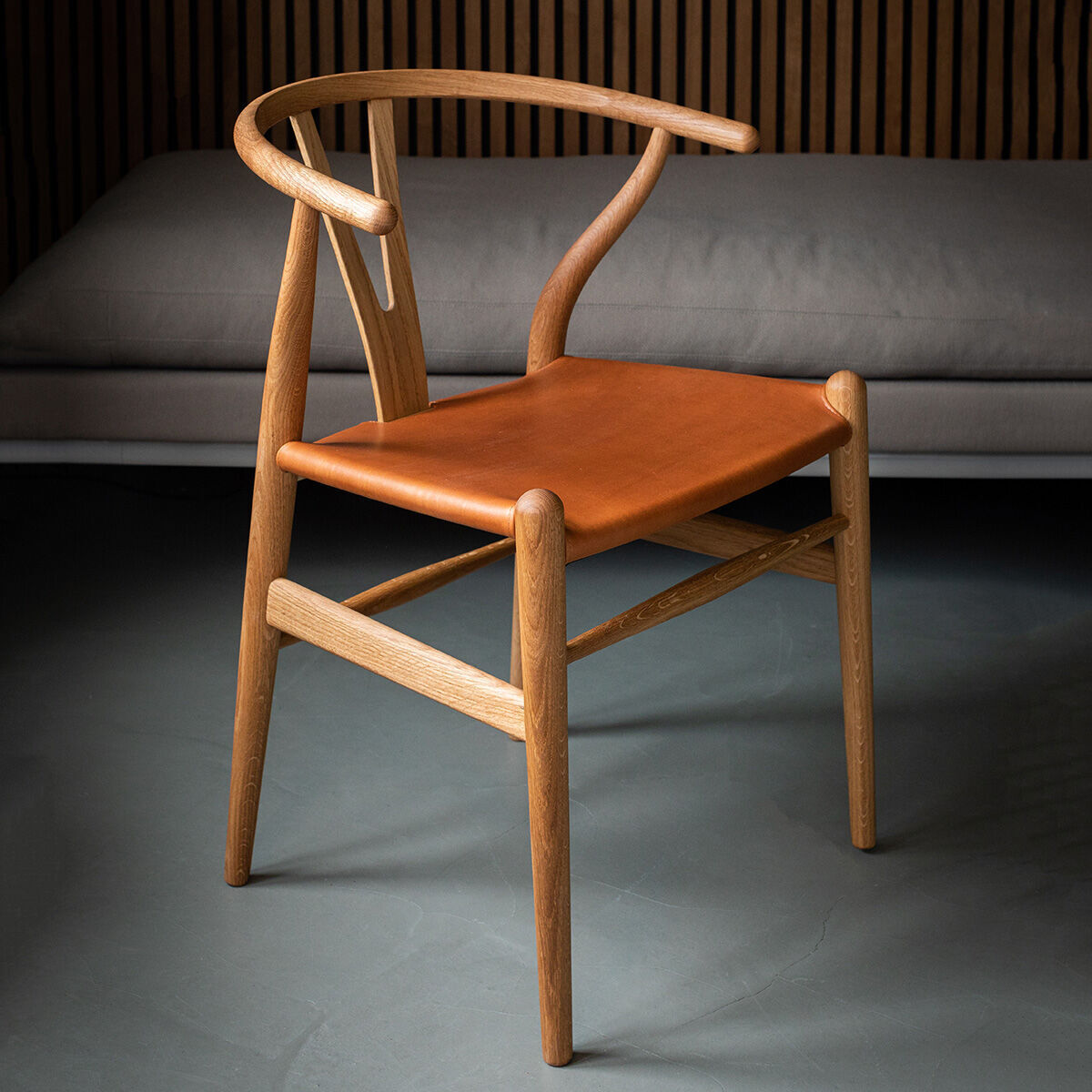 Ein Wishbone Chair aus Eichenholz und Leder der Sonderedition ZEIT, mit geschwungenem Design, natürlicher Holzmaserung und einem eleganten Ledersitz, vor einer modernen Innenraumkulisse.