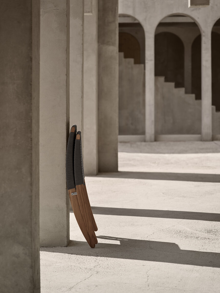 Zwei übereinander gestapelte Outdoor-Stühle der Marke 'MG501 Cuba Chair' aus Holz und geflochtenem Material stehen in einer modernen, betonierten Umgebung mit Säulen und Treppen im Hintergrund.