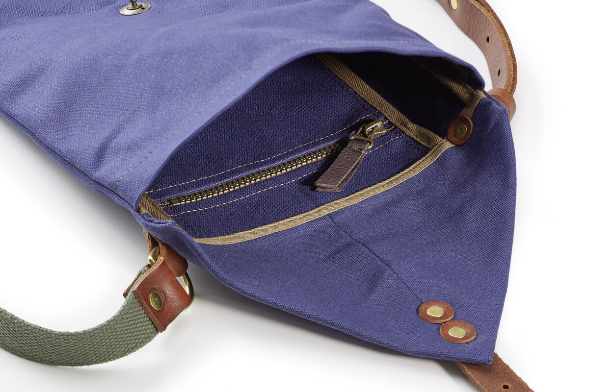Eine Map Tasche aus Canvas mit blauem Stoff und braunen Lederdetails. Sie verfügt über einen Reißverschluss und Druckknöpfe. Ideal für Outdoor-Aktivitäten.