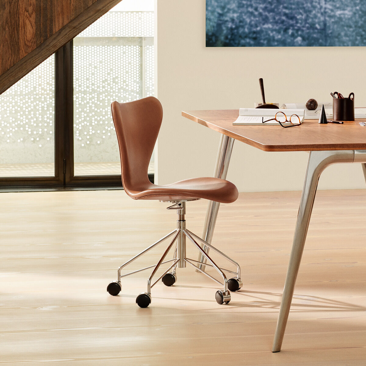 Ein stilvoller Bürostuhl der Serie 7™ in einem modern eingerichteten Büro. Der Stuhl ist drehbar und aus braunem Holz, mit einer minimalistischen und zeitlosen Form. Er steht neben einem Holzschreibtisch mit Büromaterialien.