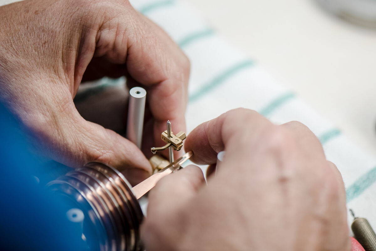 Nahaufnahme von Händen, die sorgfältig an einem kleinen, filigranen Instrument, einem Raumklimamesser, arbeiten. Das Gerät besteht aus Metall und zeigt Präzisionsarbeit und manuelle Fertigung.