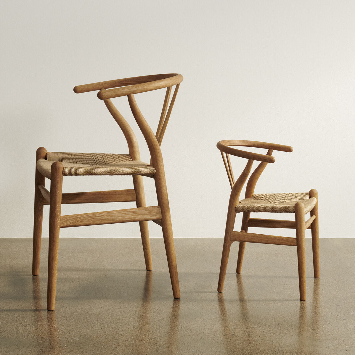 Zwei Wishbone Stühle in einer minimalistischen Umgebung. Einer der Stühle ist kleiner und für Kinder gedacht.