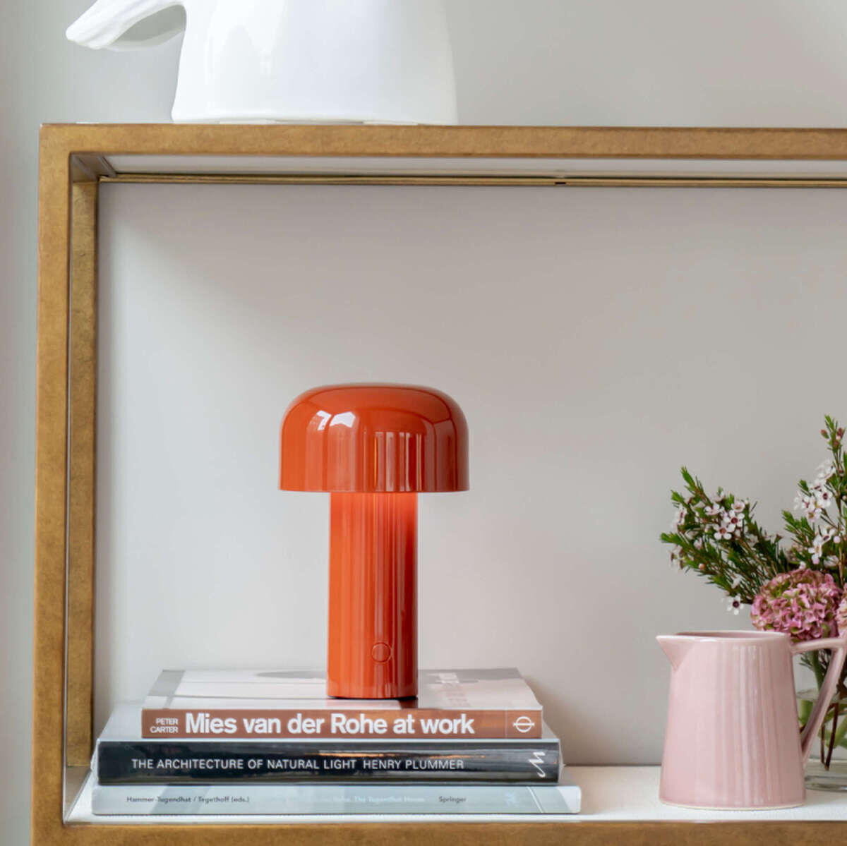 Rote Tischleuchte Bellhop auf einem Regal neben Büchern und einer kleinen Vase mit Blumen, stilvolles und minimalistisches Design.