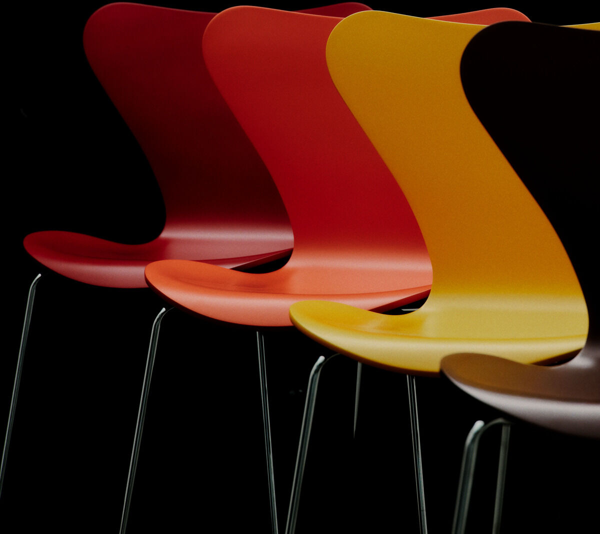 Vier stapelbare Stühle aus der Serie 7 Edition Verner Panton von Fritz Hansen stehen leicht versetzt nebeneinander. Die Sitzschalen sind aus lackiertem Buchenfurnier in Rot- und Gelbtönen mit schlanken Stahlrohrgestellen vor schwarzem Hintergrund arrangiert.