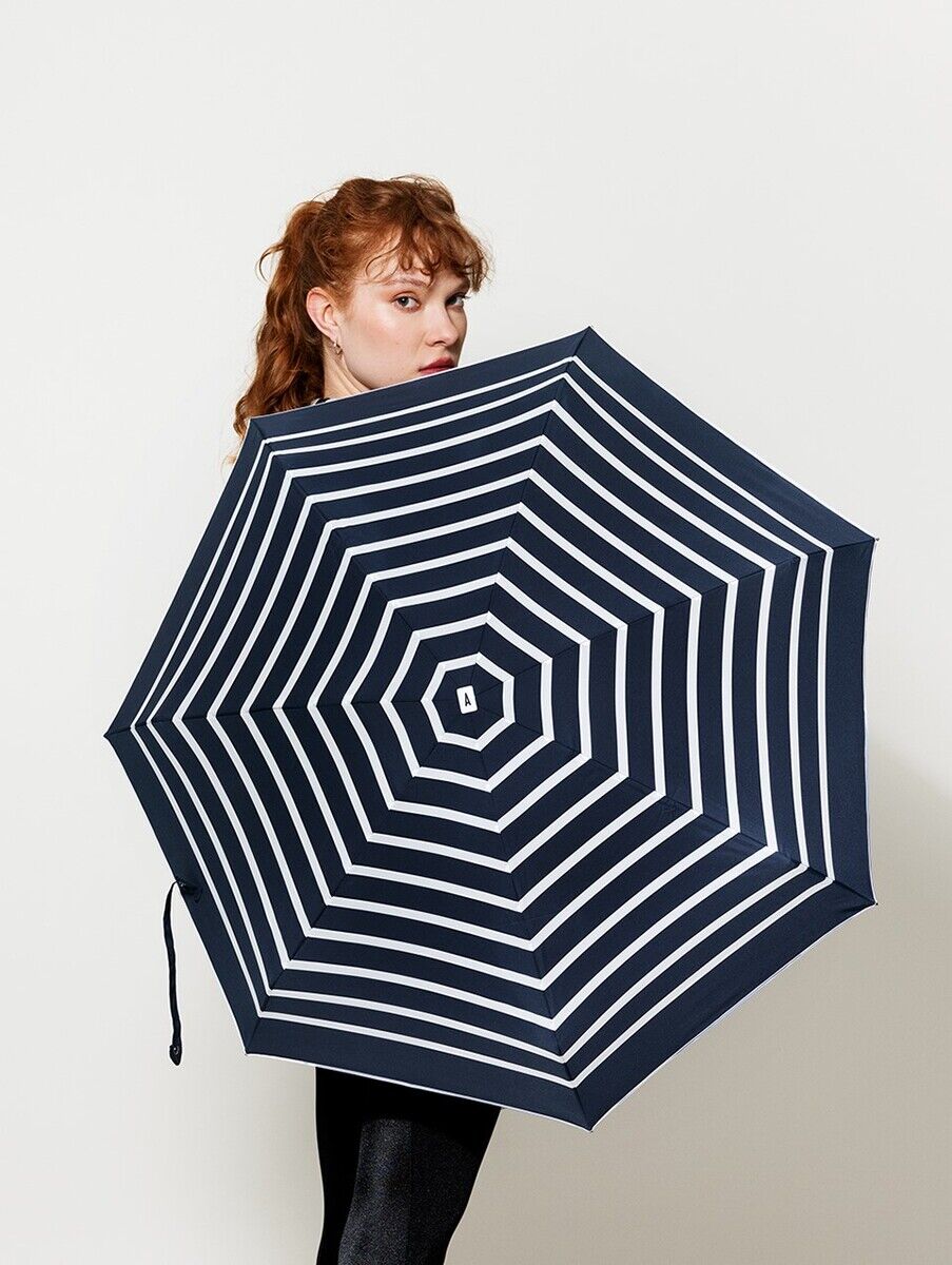Eine Frau mit roten Haaren hält einen Taschenschirm in Navy mit elfenbeinfarbenen Streifen vor ihrem Körper.