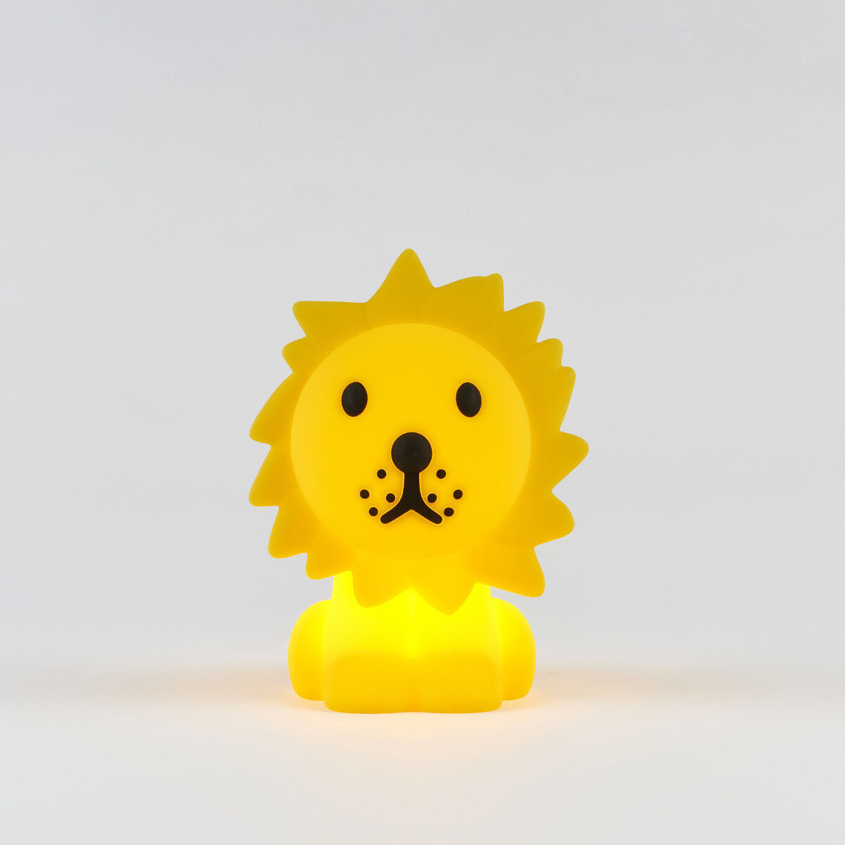 Ein kleines, gelbes Nachtlicht in Form eines sitzenden Löwen mit schwarzen Augen und Nase, ideal für das Kinderzimmer.