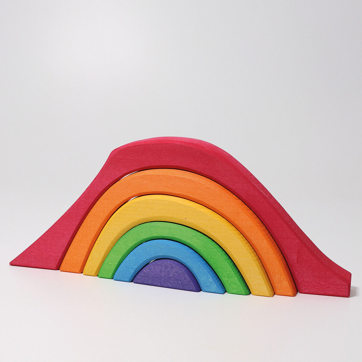 Ein bunter Baukasten in Form eines Regenbogens, bestehend aus mehreren verschiedenfarbigen Holzstücken. Die Bögen sind in Rot, Orange, Gelb, Grün, Blau und Violett gehalten und aufeinander gestapelt.