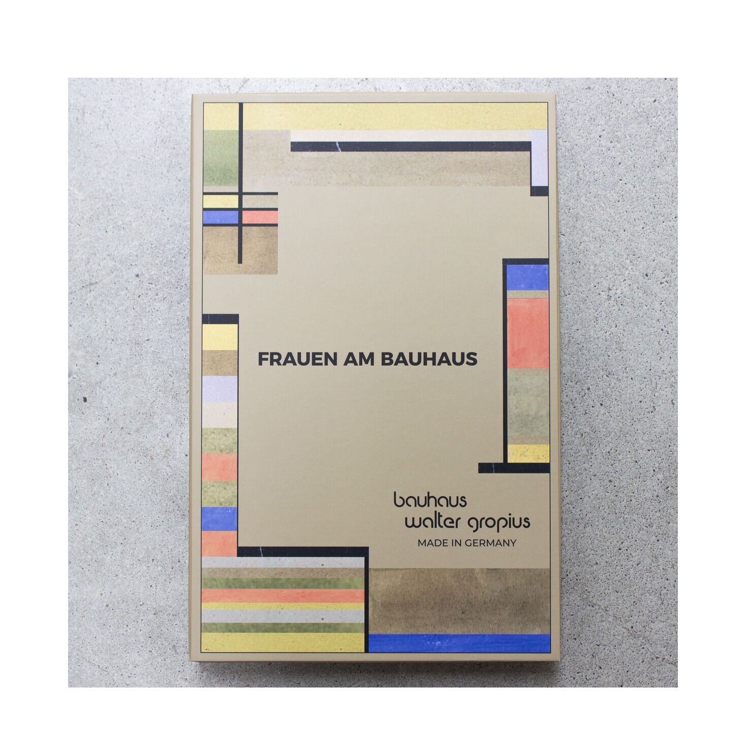 Rechteckige Verpackung der ZEIT-Sonderedition Uhr »Frauen am Bauhaus« von Walter Gropius. Die Box ist beige mit typischen geometrischen Bauhaus-Farbfeldern in Rot, Blau, Grün, Gelb und Schwarz. Mittig stehen Titel und Markenname, im Hintergrund strukturierter Betonboden.