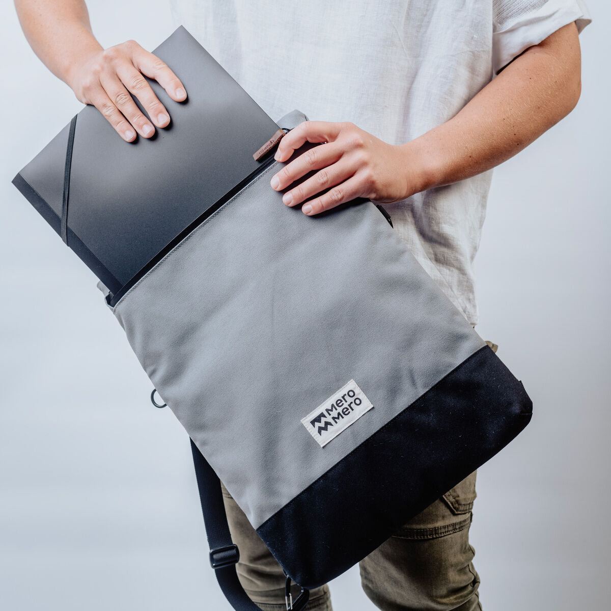 Person hält eine graue und schwarze Pouch »Meije« mit einem schwarzen Laptop, wobei die Pouch eine minimalistische und moderne Gestaltung hat.