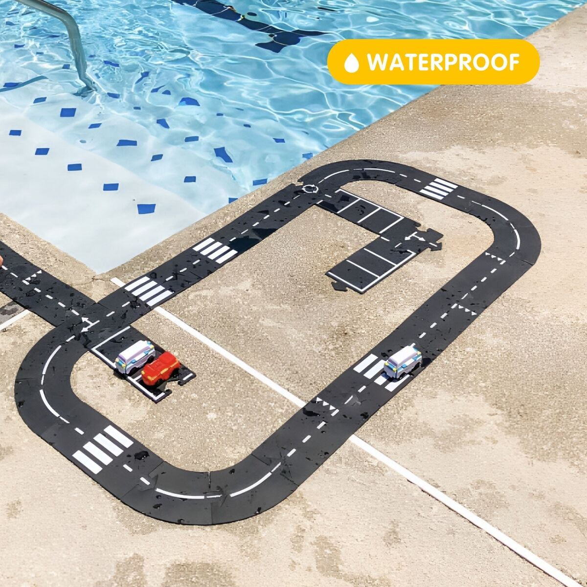 Kind spielt am Beckenrand eines Schwimmbeckens mit einem wasserdichten Straßenbau-Set »King of the road«, auf dem schwarze Fahrbahnteile mit weißen Markierungen und mehrere kleine Spielzeugautos zu sehen sind.