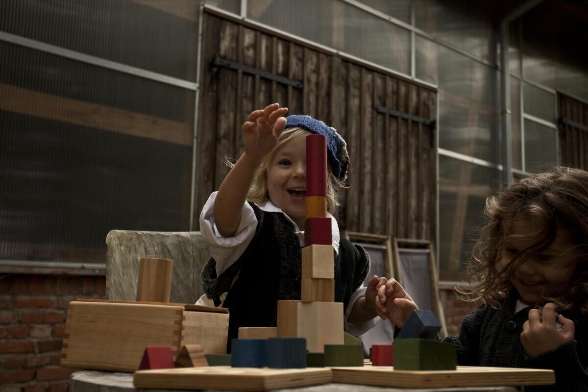 Kinder spielen begeistert mit bunten Regenbogen-Holzbausteinen in einem rustikalen Innenraum. Ein Augenmerk liegt auf dem kindlichen Spielvergnügen und der Kreativität mit umweltfreundlichen Spielzeug.