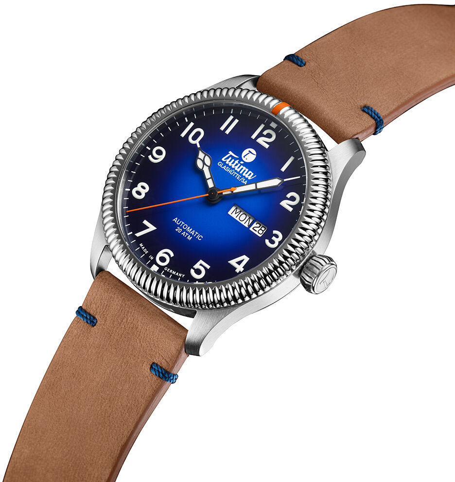 Abgebildet ist die ZEIT-Sonderedition Uhr »Grand Flieger Classic Automatic« von Tutima Glashütte: ein hochwertiger Zeitmesser mit blauem Dégradé-Zifferblatt, silbernem Edelstahlgehäuse, orangem Sekundenzeiger und cognacfarbenem Lederarmband mit blauen Nähten.