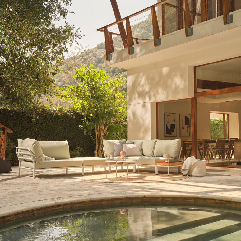 Ein moderner Loungesessel Modell LEVEL 2 steht auf einer Terrasse mit Blick auf eine üppige grüne Landschaft. Die Terrasse ist mit weiteren Gartenmöbeln ausgestattet, darunter ein Sofa und ein kleiner Tisch. Die Umgebung strahlt Ruhe und Entspannung aus.