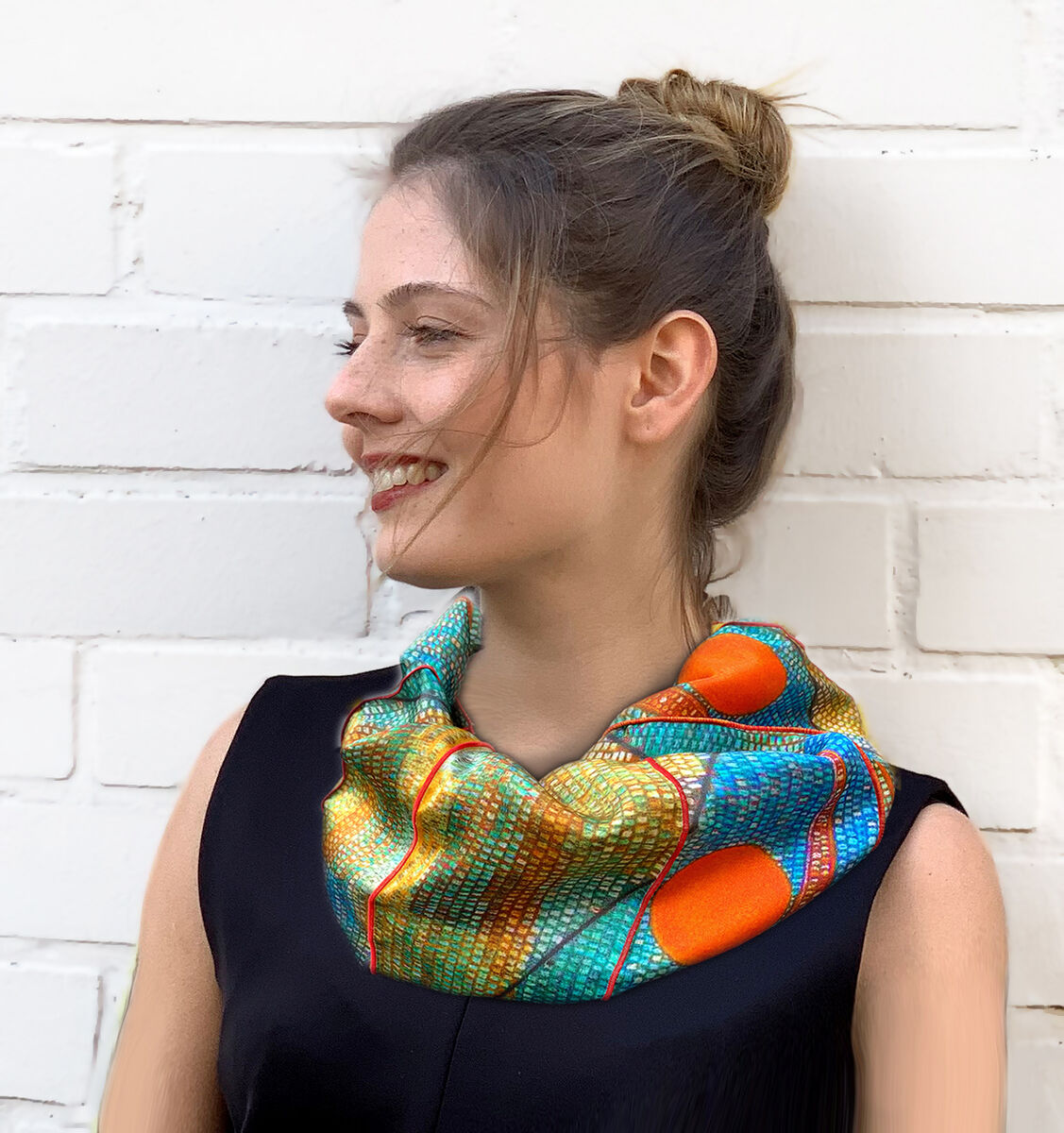 Junge Frau mit einem farbenfrohen Rundschal im geometrischen Muster, inspiriert vom Gemälde 'Ad Parnassum' von Paul Klee, vor einer weißen Ziegelwand.