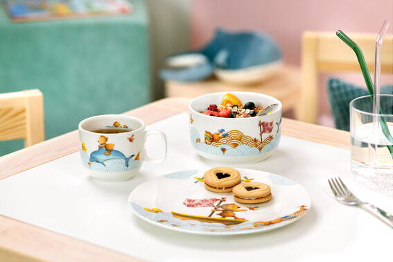 Kindergeschirr-Set 'Hungry as a Bear', bestehend aus einer Tasse, einer Schale und einem Teller mit buntem Tiermotiv, auf einem weißen Tisch in einer kinderfreundlichen Umgebung.