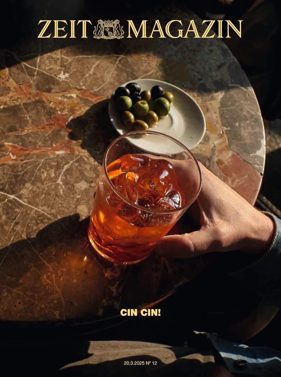 Titelbild des ZEIT Magazins Ausgabe 12/2025. Ein Cocktail in einem Glas steht auf einem Steintisch im Sonnenlicht. Eine Hand hält das Glas. Daneben steht ein Teller mit Oliven. Die Szene erzeugt eine stimmungsvolle Atmosphäre zwischen Licht und Schatten.