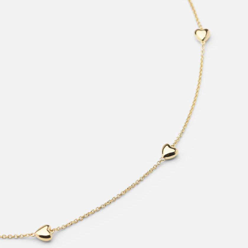 Feines Collier aus vergoldetem 925er Sterlingsilber mit vier dezenten goldenen Herzanhängern, zart an einer filigranen Kette arrangiert. Die Kette liegt auf weißem Untergrund und wirkt elegant, leicht und modern mit sanftem Glanz.