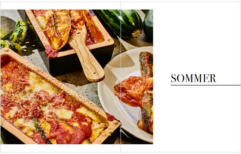 Das Bild zeigt eine Doppelseite aus dem Kochbuch »Frisch vom Wochenmarkt«. Auf der linken Seite sieht man zwei Lasagne-Gerichte in backofenfesten Formen. Die Lasagne ist mit einer goldbraunen Kruste aus Käse bedeckt und von roter Tomatensauce durchzogen. Daneben liegt ein hölzerner Pfannenwender. Die rechte Seite zeigt den Titel 'Sommer' auf weißem Hintergrund sowie ein weiteres Lasagne-Gericht auf einem Teller. Im Hintergrund sind Zucchini zu sehen.