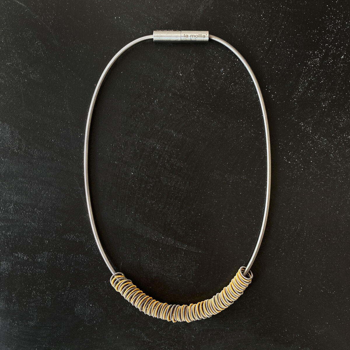 ZEIT-Sonderedition Collier bestehend aus einer silbernen Halskette mit goldenen Verzierungen auf schwarzem Hintergrund.