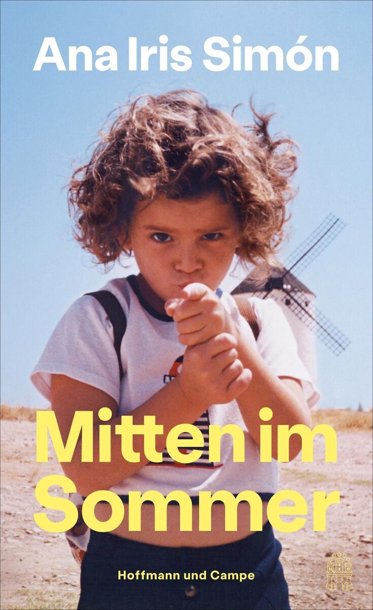 Das Cover des Buches 'Mitten im Sommer' von Ana Iris Simón zeigt ein Kind mit lockigem Haar und ernster Miene, das einen Finger in die Kamera streckt. Im Hintergrund steht eine Windmühle vor einem klaren blauen Himmel. Der Titel des Buches und der Name der Autorin sind in weißer und gelber Schrift abgedruckt.