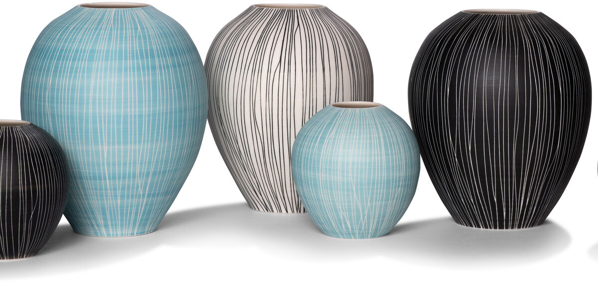Eine Gruppe von sechs kleinen Keramikvasen in verschiedenen Größen. Die Vasen sind in den Farben Schwarz, Blau und Weiß mit feinen Streifenmustern gestaltet. Die größte Vase ist blau und links positioniert, während die kleinste Vase schräg rechts vorne steht.