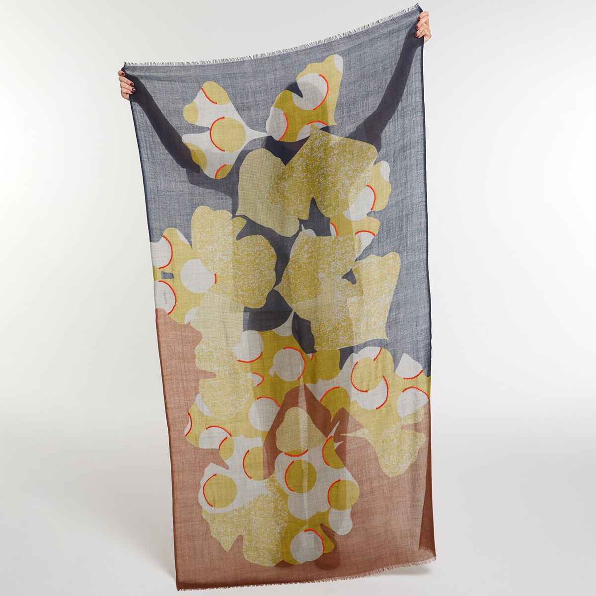 Wollschal 'Eternel' in Blau und Rot mit aufgesticktem floralen Design aus gelben, weißen und roten Elementen. Der großformatige Schal wird mit zwei Händen in die Kamera gehalten, der Hintergrund ist neutral weiß. Das Accessoire eignet sich für modische Outfits und als Geschenk.