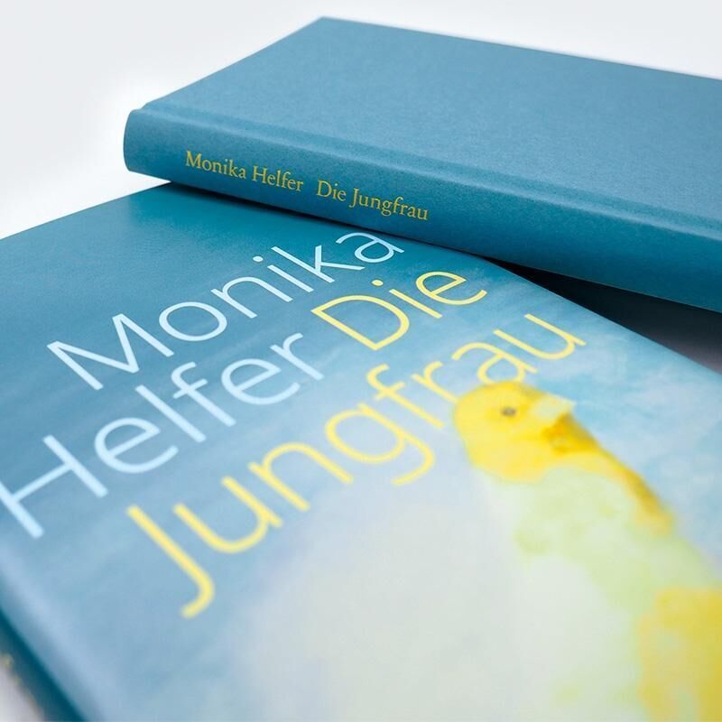 Das Bild zeigt das Buchcover von 'Die Jungfrau' von Monika Helfer. Das Buch hat einen blauen Einband mit gelber und weißer Schrift und einem verschwommenen gelben Bild.