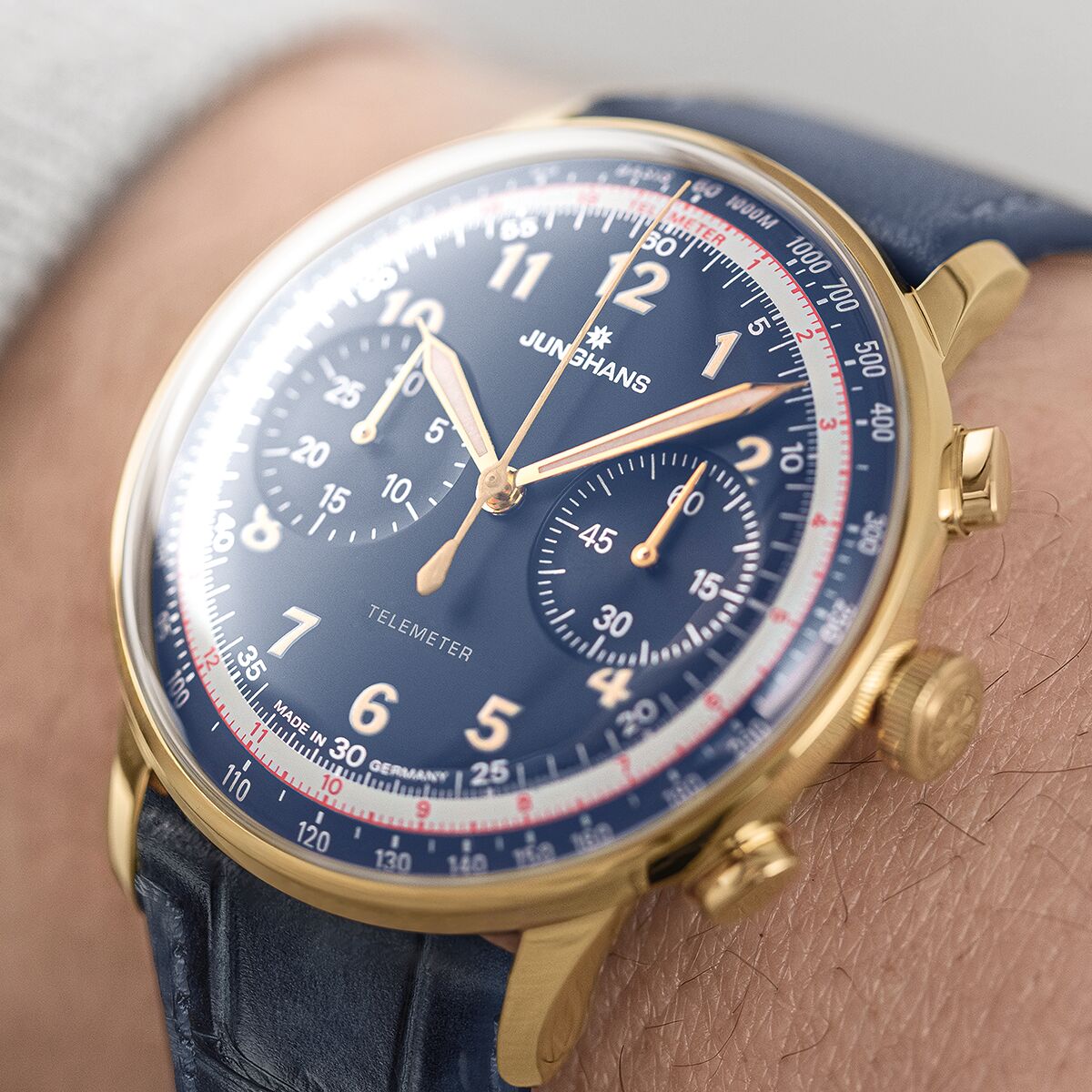 Nahaufnahme einer klassischen Armbanduhr der ZEIT-Sonderedition »Telemeter« von Junghans mit rundem goldfarbenem Gehäuse, blauem Zifferblatt, weißen und roten Skalen sowie blauem Lederarmband. Die Uhr trägt moderne und elegante Züge und ist für besondere Anlässe geeignet.